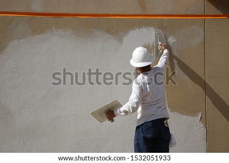 Stucco on a building wall. An unidentifiable contractor applies Stucco or Wall Texture to the outside of a building wall in preparation of painting the building. Wall and Building Repair and Patching  Royalty-Free Stock Photo #1532051933