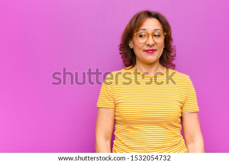 middle age woman wondering, thinking happy thoughts and ideas, daydreaming, looking to copy space on side against purple wall