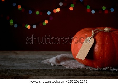 Autumn background on dark wooden surface, orange pumpkin on a background of blurry lights, selective focus