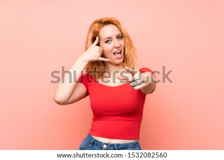 Young woman over isolated pink background making phone gesture and pointing front