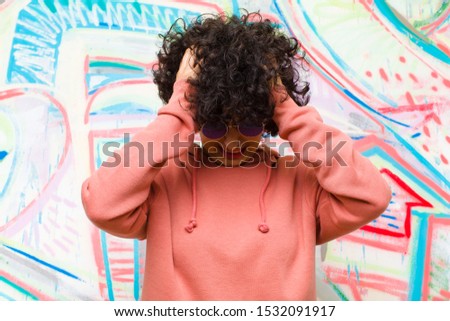 young pretty afro woman feeling stressed and frustrated, raising hands to head, feeling tired, unhappy and with migraine against graffiti wall