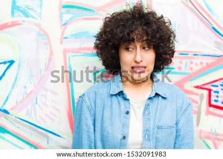 young pretty afro woman looking worried, stressed, anxious and scared, panicking and clenching teeth against graffiti wall