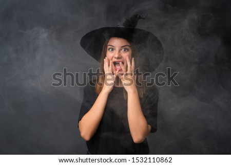 Girl with witch costume for halloween parties over isolated dark background with surprise facial expression