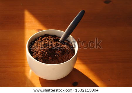 White bowl with ground coffee and spoon on wooden table.
