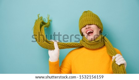 Winter portrait of happy young woman wearing knitted hat, scarf and sweater. Girl having fun on bright teal background. Fashion concept.                                