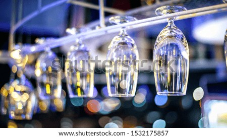 Empty wine glasses  hanging up side down above a bar rack in night club