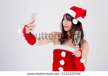 Beautiful portrait young asian woman in Santa holding glass of champagne and selfie with phone in party celebrating in xmas holiday isolated on white background, Christmas and new year concept.