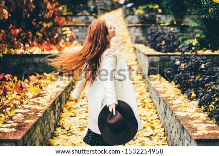 Beautiful woman with the hats enjoying autumn. Trendy red hair woman in fall at the park. Concept of autumn mood.