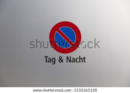 Parking forbidden German sign, at a silver garage door, German translation: day and night