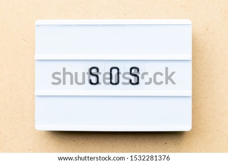 White lightbox with word SOS (abbreviation of save our soul/ship or sibling over shoulder) on wood background
