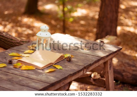 notebook with yellow autumn leaves, cones and a white lantern on a wooden surface in the forest