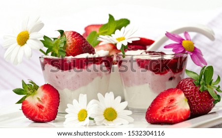 Healthy breakfast: close up of two glasses with natural yoghurt, curd, fresh, fruity strawberries,  served on a wooden white table with tablecloth , decorated with white and pink daisies.