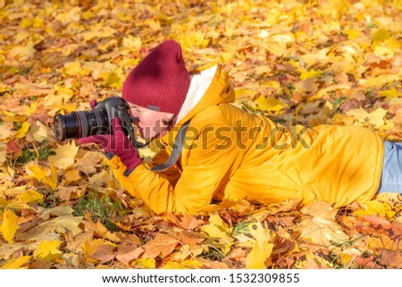 Photographer woman lies on autumn grass wuih a camera in her hands for taking pictures