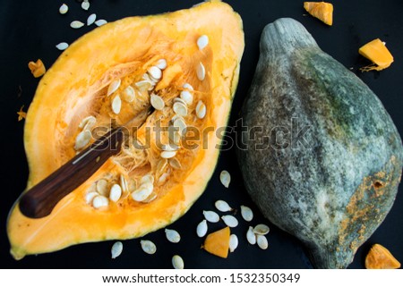 Two halves of a pumpkin with seeds, fruit pieces and interesting surface against black background
