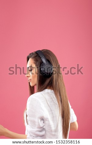 Beautiful woman listening to music using wireless headphones in studio isolated over pink background.Girl enjoying wireless earphones