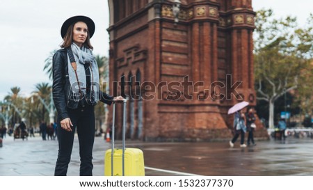 Photographer tourist with photo camera. Girl in hat with suitcase travels in Triumphal arch Barcelona. Holiday concept in europe street. Traveler hipster shoot architecture city