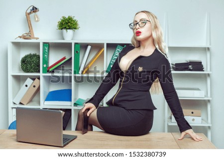 Young woman with big breasts sits on a table in an office near a laptop.