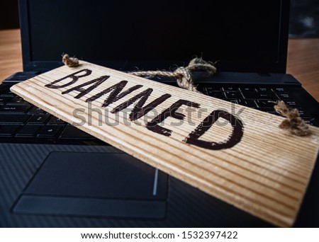 turned off laptop with a wooden sign that says banned