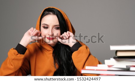 Close up shot of beautiful teenage girl forcing a smile, holding her fingers at the edges of her lips, looking at the camera. Body language