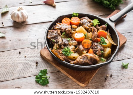 Beef meat stewed with potatoes, carrots and spices on wooden background, copy space. Homemade winter comfort food - slow cooked meat stew. Royalty-Free Stock Photo #1532437610