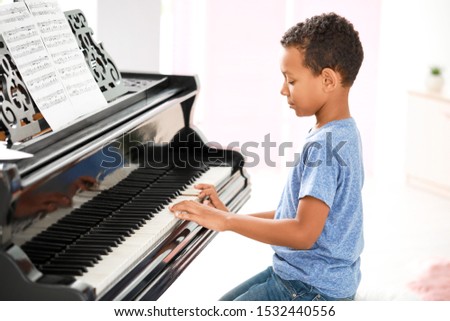 Little African-American boy playing grand piano at home
