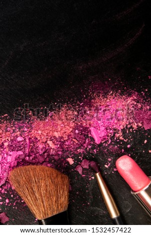 Make-up brushes, lipstick, and crushed cosmetics, overhead shot on a black background texture with a copy space, a beauty design template for a makeup banner
