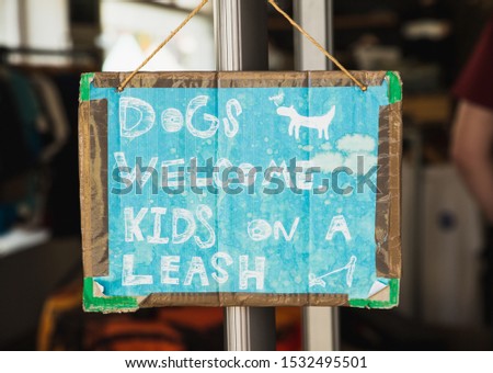 Dogs welcome, but kids on a leash please illustrated on the front door of a shop for tourists in Cornwall England. comedy enticing customers to come in and visit the shop. Funny sign by shop keeper