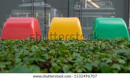 Red yellow and green plastic trash bin behind bush