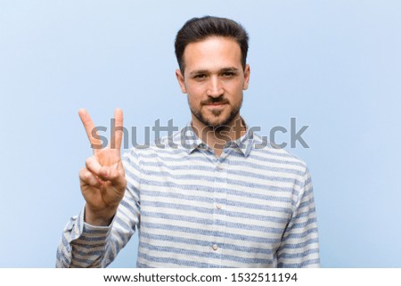 young handsome man smiling and looking friendly, showing number two or second with hand forward, counting down
