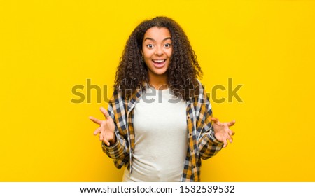 young pretty african american woman feeling happy, astonished, lucky and surprised, like saying omg seriously? Unbelievable against yellow wall