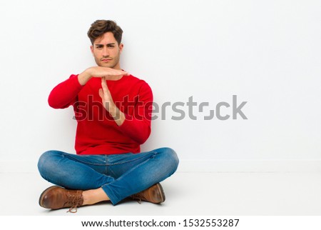 young handsome man looking serious, stern, angry and displeased, making time out sign sitting on the floor