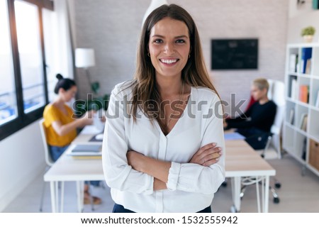 Portrait of pretty young businesswoman looking at camera. In the background, her colleagues working in the office. Royalty-Free Stock Photo #1532555942