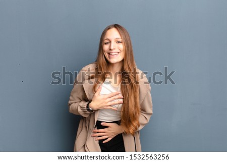 young pretty woman laughing out loud at some hilarious joke, feeling happy and cheerful, having fun against gray background
