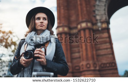Photographer tourist with retro photo camera. Girl in hat travels in Triumphal arch Barcelona. Holiday concept in europe street. Traveler hipster shoot architecture city, copy space mockup