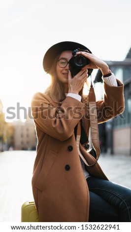 Photographer tourist with suitcase take photo on retro camera. Smiling girl in hat travels in Barcelona. Sunlight street in europe city. Traveler hipster shooting architecture, copy space mockup