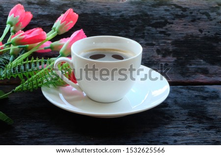 Hot coffee mugs and red flowers on a brown wooden table background