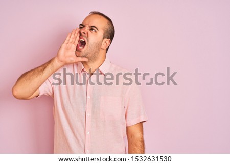 Young man wearing elegant shirt standing over isolated pink background shouting and screaming loud to side with hand on mouth. Communication concept.