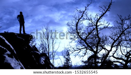 Male hiker with backpack on a mountain range cliff behind a city looking at rugged winter landscape enjoying weekend.Old trees, relaxing, freedom, silence and calm,sunset,loneliness.Composite photo.
