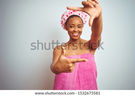 African american woman wearing pink shower towel after bath over isolated background smiling making frame with hands and fingers with happy face. Creativity and photography concept.