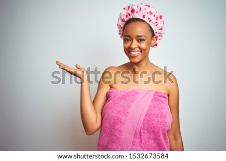 African american woman wearing pink shower towel after bath over isolated background smiling cheerful presenting and pointing with palm of hand looking at the camera.