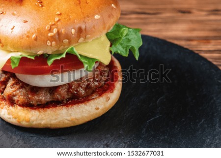 Fresh homemade burger with meat cutlet, tomatoes, lettuce, cheese and onions on a slate dish on a wooden background, close up