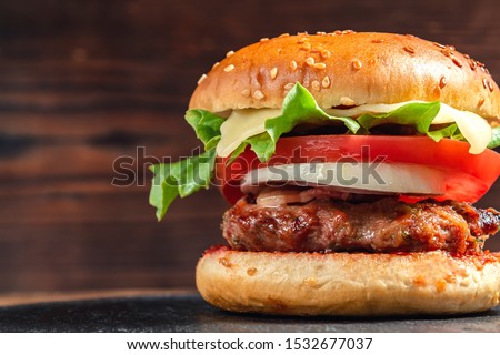 Fresh homemade burger with meat cutlet, tomatoes, lettuce, cheese and onions on a slate dish on a wooden background