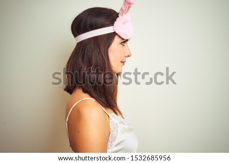 Young beautiful woman wearing pajama and mask standing over white isolated background looking to side, relax profile pose with natural face with confident smile.