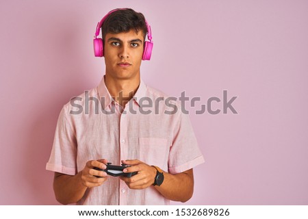 Indian gamer man playing video game using headphones over isolated pink background with a confident expression on smart face thinking serious