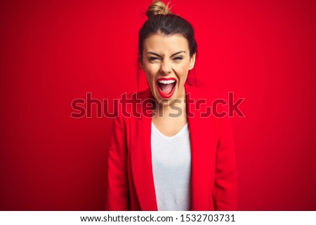 Young beautiful business woman standing over red isolated background angry and mad screaming frustrated and furious, shouting with anger. Rage and aggressive concept.
