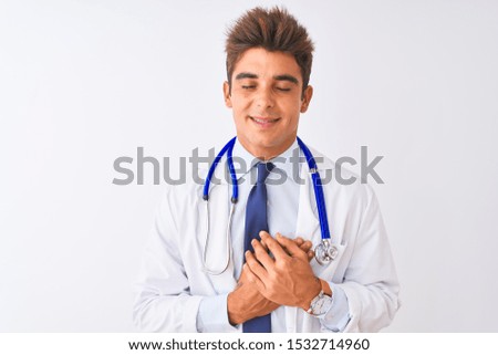 Young handsome doctor man wearing stethoscope over isolated white background smiling with hands on chest with closed eyes and grateful gesture on face. Health concept.