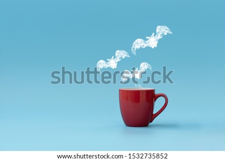 Steam in three bats shape flying from coffee cup against blue background. Morning drink. Halloween celebration concept. Copy space