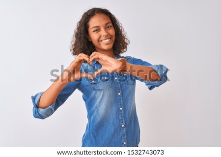 Young brazilian woman wearing denim shirt standing over isolated white background smiling in love doing heart symbol shape with hands. Romantic concept.