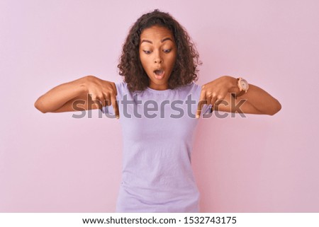 Young brazilian woman wearing t-shirt standing over isolated pink background Pointing down with fingers showing advertisement, surprised face and open mouth
