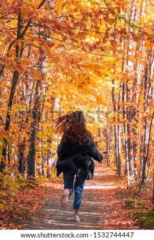 Young female running in the woods in a beautiful path with beautiful, colorful fall foliage all around her. Shot in Bromont, Quebec, Canada. 